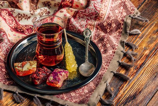 Tea in armudu glass with oriental delight rahat lokum on metal tray over wooden surface and tablecloth