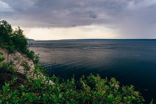 Overcast sky over the river. Cliff with bushes