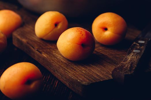 Mellow apricots with knife over old wooden cutting board and metal bowl with fruits