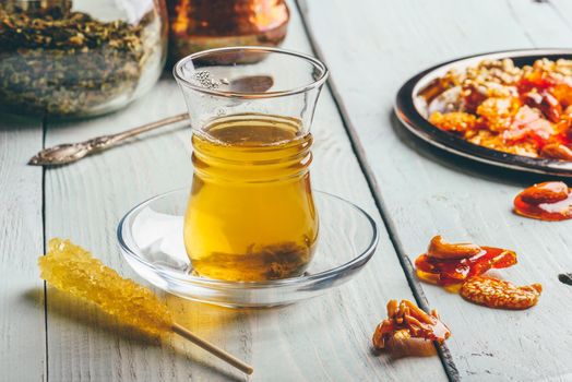 Herbal tea in oriental glass with arabian nut delights on metal plate over light wooden surface