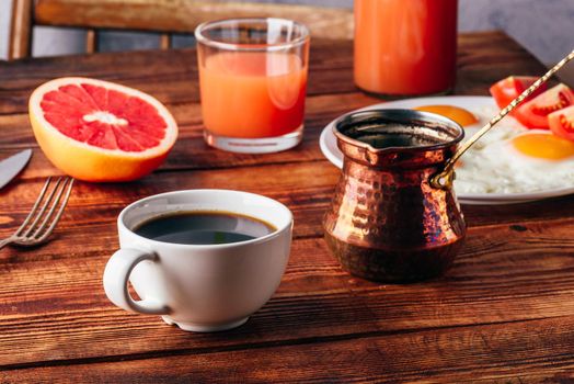 Breakfast with turkish coffee, fried eggs, juice and fruits over wooden table