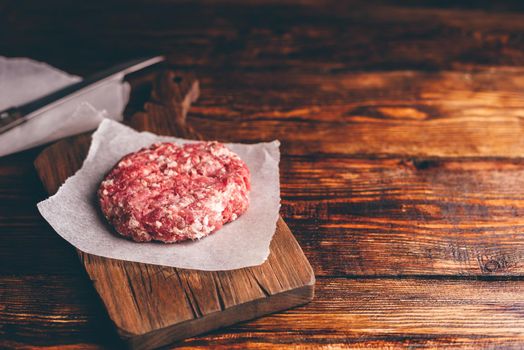 Raw Pork Patty for Burger on Cutting Board and Wax Paper. Copy Space on the Right.