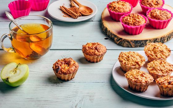 Healthy Breakfast. Cooked oatmeal muffins with apple and cup of green tea over light wooden background.