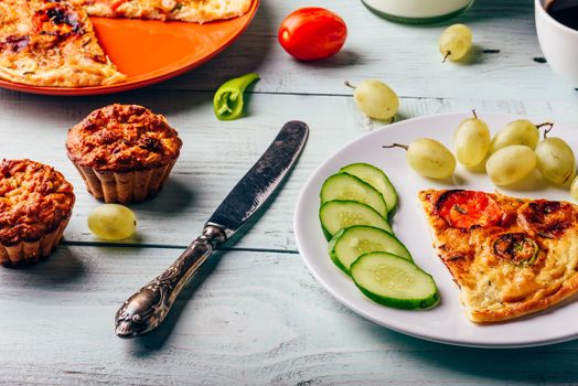 Frittata with chorizo, tomatoes and chili peppers on plate and muffins over light wooden background.