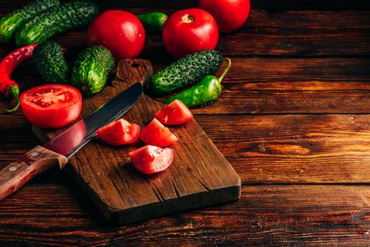 Sliced tomatoes on cutting board and cucumbers with chili peppers over wooden background.