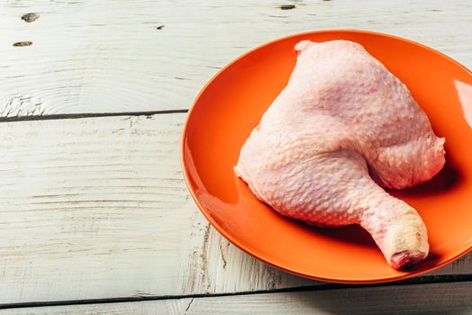 Chicken leg on orange plate over light wooden surface