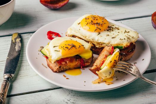 Sandwiches with vegetables and fried egg on white plate, cup of coffee and some fruits over wooden background.