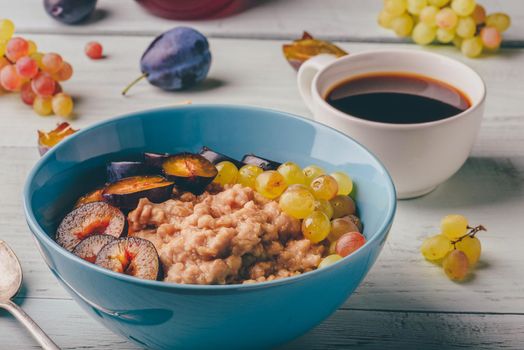 Healthy breakfast concept. Porridge with fresh plum, green grapes and cup of coffee. Ingredients over wooden background.