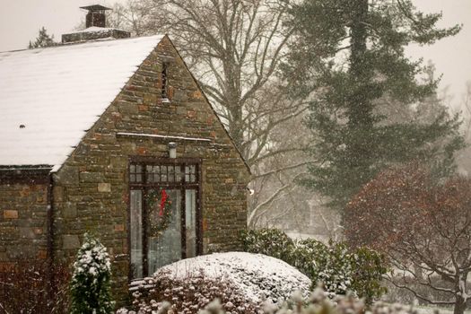 A Cobblestone Home With a Wreath in a Window next to a Suburban Street During a Snowstorm