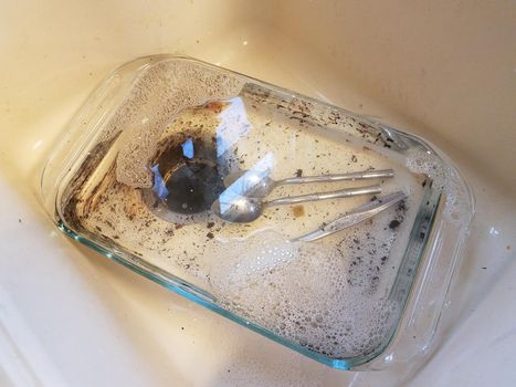 dirty glass tray in sink with water and silverware utensils