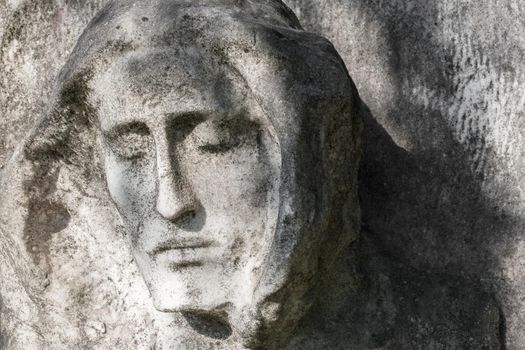 Antique stone statue of Jesus Christ, against a background of gray stone.