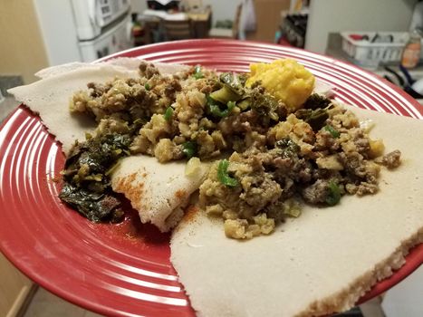 Ethiopian food spicy beef and intestine and vegetables and bread on red plate in kitchen