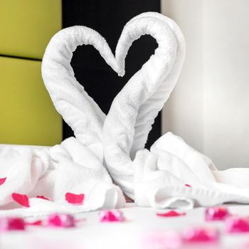 Towel swans on the bed, sprinkled with pink petals. Ideal for events and concepts, Valentine's Day, honey moon, romantic week end and more.