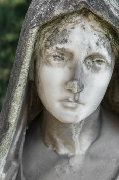 Ruined face of a statue of Virgin Mary. In the face the signs of the passing of time. Mold appears. Peace symbol.