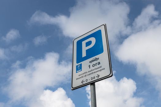 Parking sign with time limit one hour except authorized, isolated on a blue sky with white clouds.