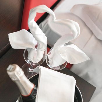 Honeymoon concept. Composition of two towel swans, wine glasses and ice bucket with champagne in hotel room. Romantic drink for lovers. Valentines day concept.