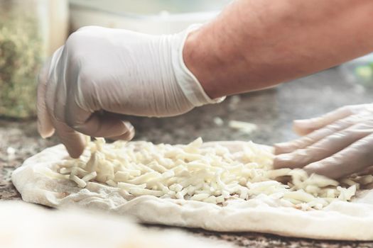 Hands with plastic gloves of pizza chef making pizza at kitchen