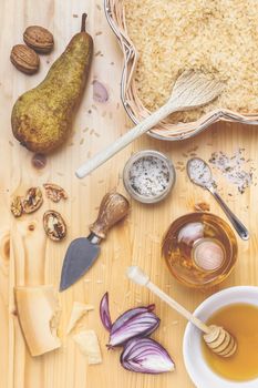 Assorted ingredients for cooking rice. Raw carnaroli rice, pears, walnuts, honey, onions, parmesan and olive oil over rustic wooden background. Top view.