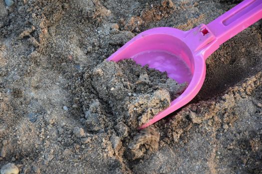 Closeup shot of a pink plastic toy shovel on sand