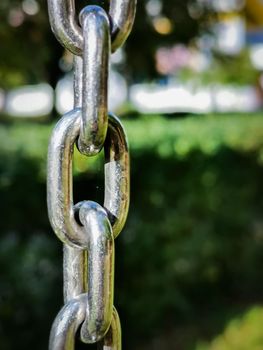 Closeup vertical shot of a metal chain swing detail in a playground with a nature background
