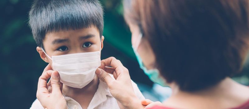 Mother take care son with face mask for protection disease flu or covid-19 outdoors, mom wearing on medical mask with child safety for protect outbreak of pandemic, medical concept, banner website.