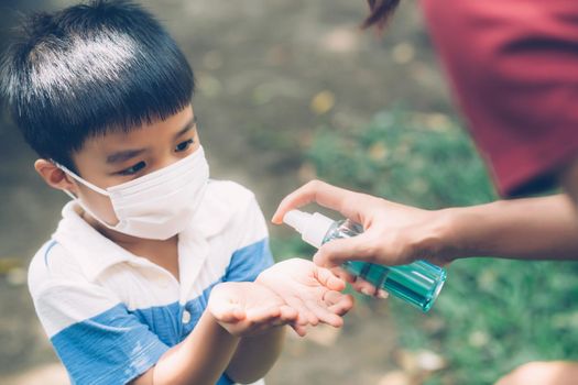 Mother take care son with face mask and sanitizer for protection disease flu or covid-19 outdoors, mom and child wearing medical mask clean hand for safety for outbreak of pandemic in public.