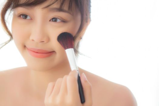 Beauty portrait young asian woman smile with face looking mirror applying makeup with brush cheek in the bedroom, beautiful of girl holding blusher, skin care and cosmetic concept.