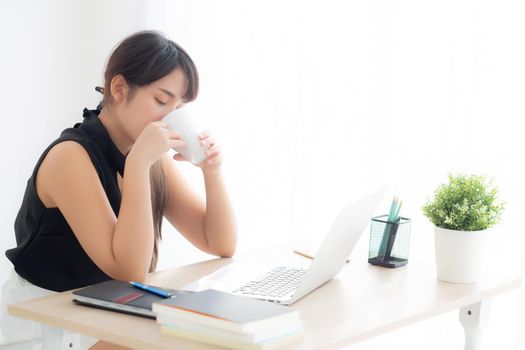 Beautiful young freelance asian woman smiling working and on laptop computer at desk office with professional, girl using notebook and drink coffee, business and lifestyle concept.