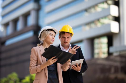 Female industrial engineer wearing a white helmet while standing in a construction site with businessman talking on working plan, Engineer and architects at construction site concept