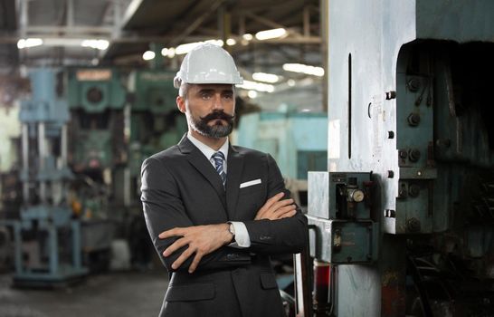 The bearded hipster director with engineer hat standing against cnc machine in production in factory