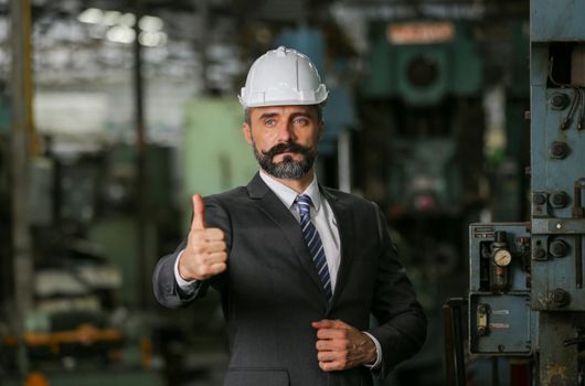 The bearded hipster director with engineer hat standing against cnc machine in production in factory