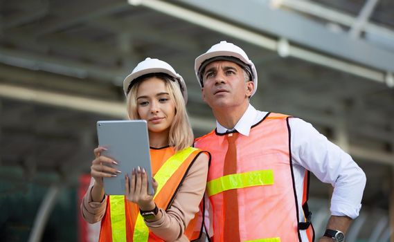 Female industrial engineer wearing a white helmet while standing in a construction site with businessman talking on working plan, Engineer and architects at construction site concept