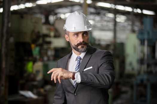 The bearded hipster director with engineer hat standing against cnc machine in production in factory