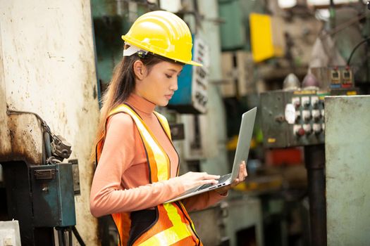 Female technician worker in uniform working on laptop with machine in manufacturing.	
