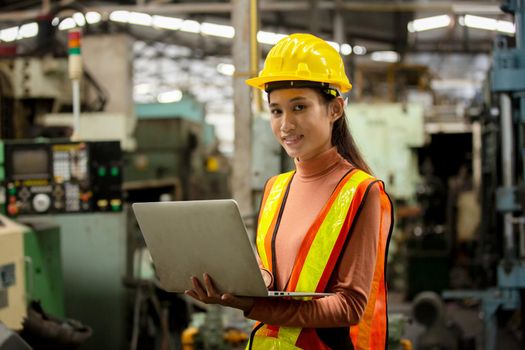 Female technician worker in uniform working on laptop with machine in manufacturing.