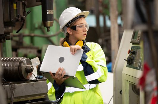 Female technician worker in uniform working on laptop with machine in manufacturing.