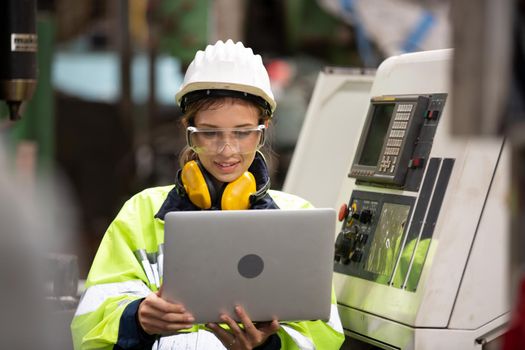 Female technician worker in uniform working on laptop with machine in manufacturing.