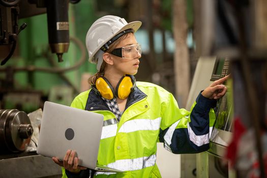 Female technician worker in uniform working on laptop with machine in manufacturing.