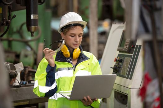 Female technician worker in uniform working on laptop with machine in manufacturing.	
