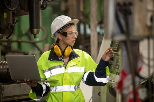 Female technician worker in uniform working on laptop with machine in manufacturing.	
