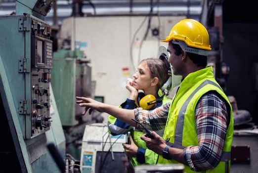 Men and female workers in factory operating machine in workshop floor.