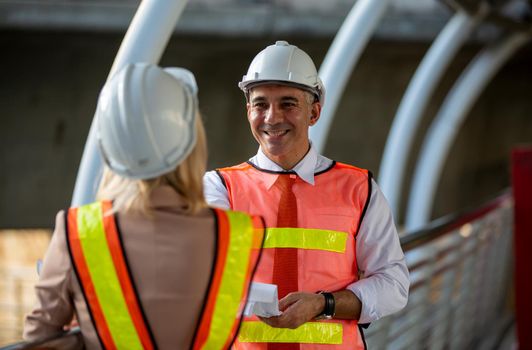 Female industrial engineer wearing a white helmet while standing in a construction site with businessman talking on working plan, Engineer and architects at construction site concept