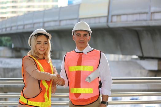 Female industrial engineer wearing a white helmet while standing in a construction site with businessman talking on working plan, Engineer and architects at construction site concept