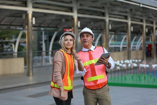 Female industrial engineer wearing a white helmet while standing in a construction site with businessman talking on working plan, Engineer and architects at construction site concept