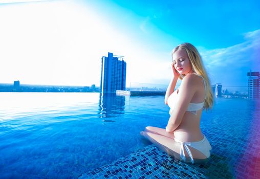 Young woman enjoying a sun, Slim young girl model in white bikini  by the pool.