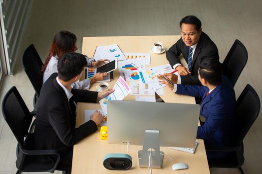 young business team working together at office. Manager pointing at a chart and explaining the analysis about business strategies. Top view shot of business hand shake