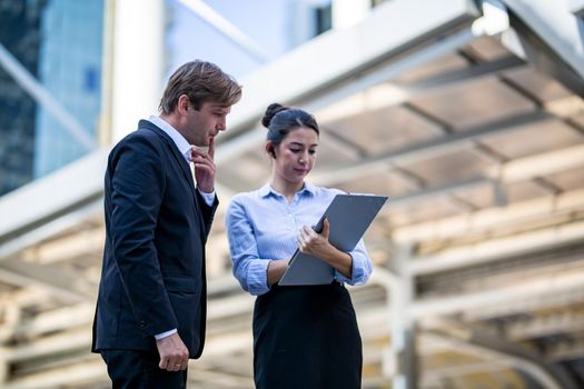 Businessman and women sitting on step outdoor looking on laptop against building