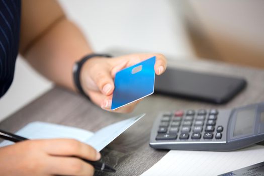 midsection of woman with credit card book bank and calculator paying bills online indoor