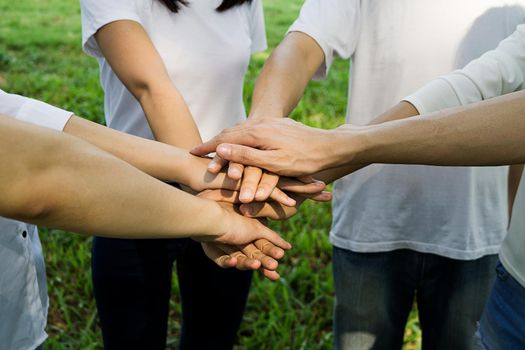 business team working at trendy loft office. Young mixed race group of people puts palm together on the centre. Teamwork of happy guys, colleagues.