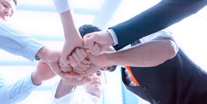 business team working at trendy loft office. Young mixed race group of people puts palm together on the centre. Teamwork of happy guys, colleagues.